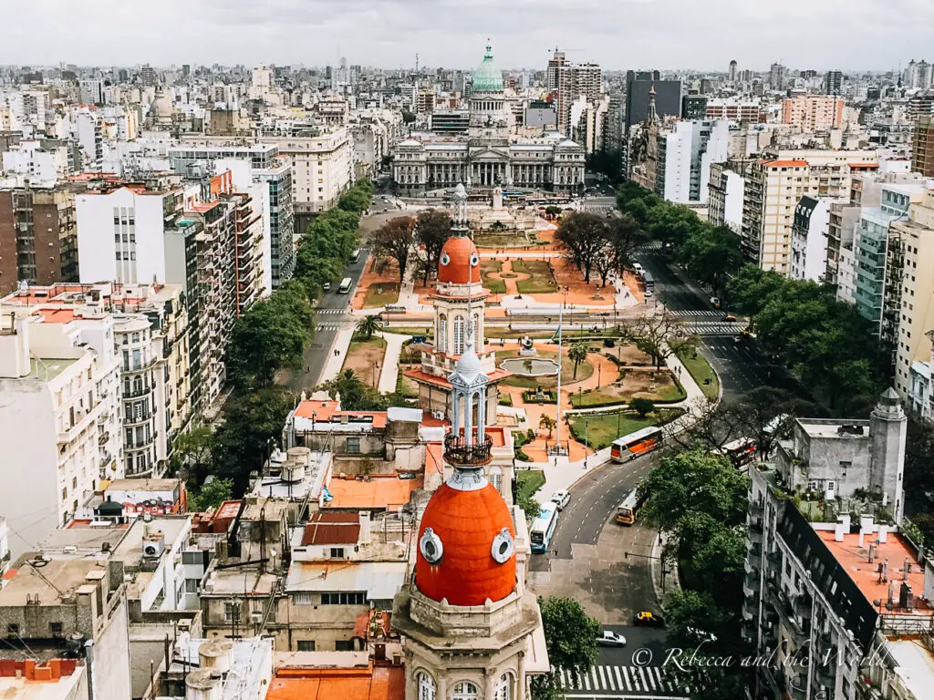 Aerial view of Buenos Aires from Palacio Barolo, showing the expansive cityscape. The foreground features the distinctive red dome of the building, with the sprawling urban grid, green park spaces, and distant buildings stretching to the horizon.